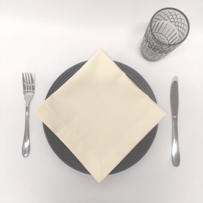 Mesa posta com talheres metálicos, guardanapo bege, prato cinzento e copo de vidro transparente