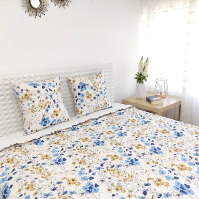 conjunto de cama com colcha e almofadas florais azuis e amarelas num quarto iluminado