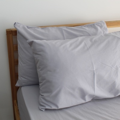 Duas almofadas cinza claro sobre cama com estrado de madeira clara