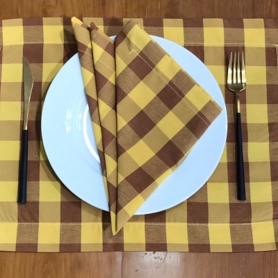 Mesa posta com jogo americano e guardanapo xadrez amarelo e castanho, prato branco e talheres pretos