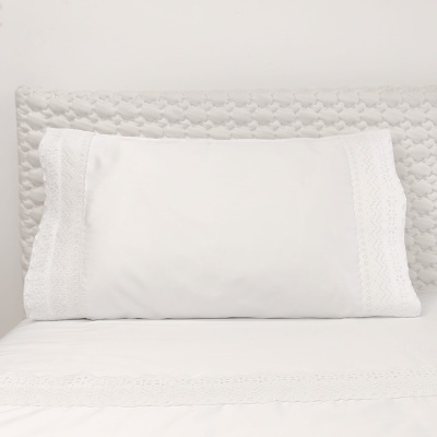 Almofada branca com bordado rendado e lençol, cama com cabeceira cinza acolchoada