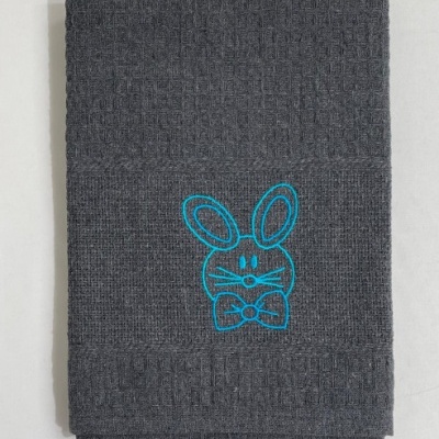 Toalha cinzenta com bordado azul de um coelho com laço