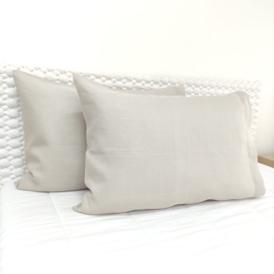 Duas almofadas bege claro sobre cama branca com cabeceira malhada