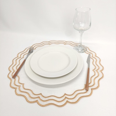 Conjunto de loiça branca com pratos, talheres com cabo de madeira, copo de vinho e individual branco com bordas douradas onduladas.