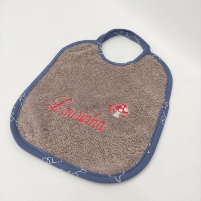 Babete castanho felpudo com bordado Vermelho e rebordo azul.