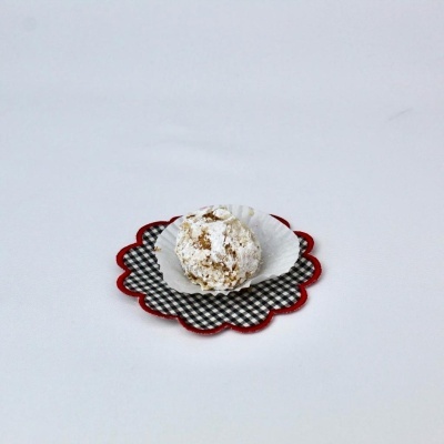 Doce redondo com açúcar em pó em forminha branca sobre suporte xadrez preto e branco com contorno vermelho