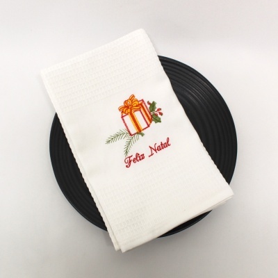 Toalha branca bordada com presente de Natal e frase Feliz Natal sobre prato preto