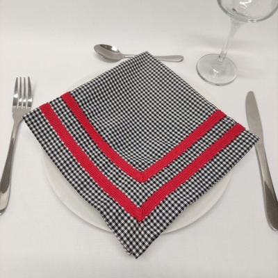 Guardanapo preto e branco com linhas vermelhas sobre prato branco com talheres e copo