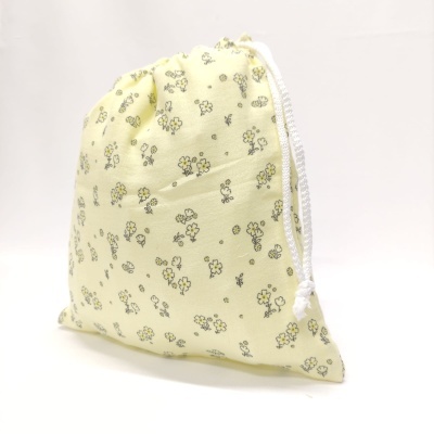 Saco de pano amarelo claro com flores e cordão branco em fundo branco