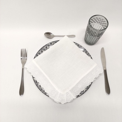 Conjunto de talheres, prato com padrão azul e branco, copo transparente e guardanapo branco bordado