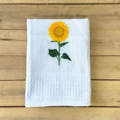 Toalha branca com bordado de girassol sobre madeira