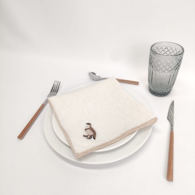 Conjunto de mesa com prato branco, guardanapo bege bordado, talheres de cabo madeira e copo de vidro texturizado