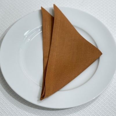 Prato branco com guardanapo castanho dobrado em triângulo sobre toalha branca