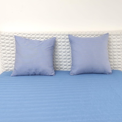 Cama com duas almofadas listradas azuis e brancas numa cabeceira branca acolchoada