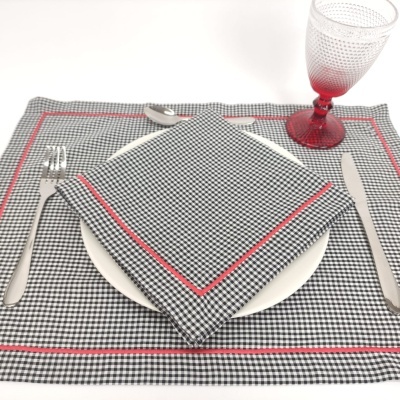 Conjunto de mesa com toalha e guardanapo xadrez, prato branco, talheres e copo vermelho
