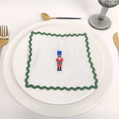 Guardanapo branco com borda verde e bordado de soldado em prato branco com talheres dourados
