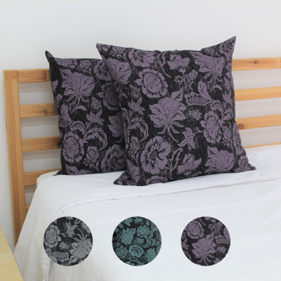 Almofadas quadradas com padrão floral roxo e preto apoiadas na cama com lençol branco