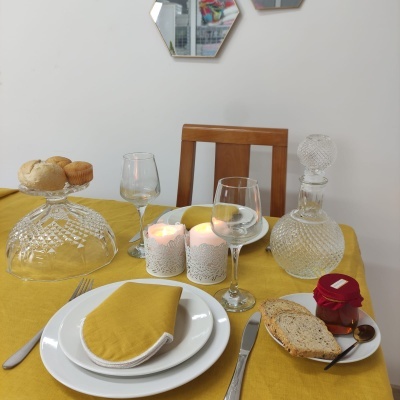 Mesa posta com toalha amarela, pratos brancos, guardanapo amarelo, copos e garrafa de vidro, velas acesas e comida sobre a mesa