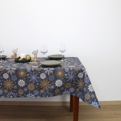 Toalha de mesa com padrão de flocos de neve azul, branco e dourado numa mesa de madeira com pratos e copos.