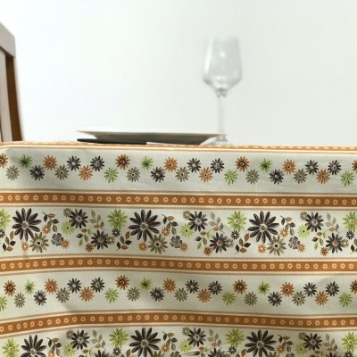Toalha de mesa com padrão floral em tons de castanho, verde e bege sobre mesa de madeira