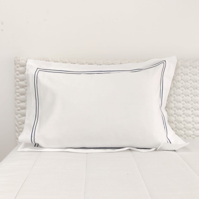 Almofada branca com bordadura cinzento escuro numa cama branca