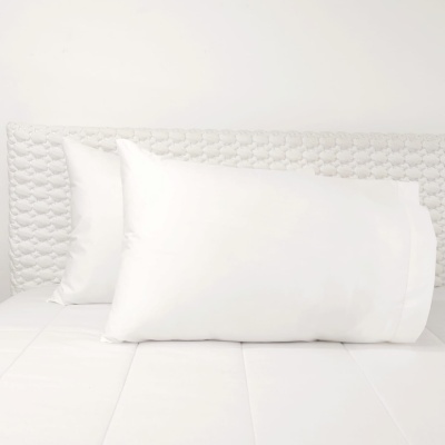 Dois travesseiros brancos sobre cama branca com cabeceira texturizada branca