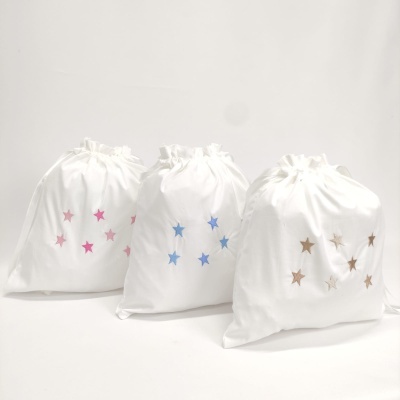 Três sacos de tecido branco com estrelas coloridas e fecho de cordão