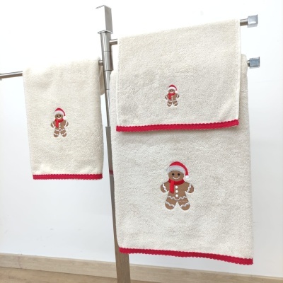 Três toalhas de banho branco com bordas vermelhas e biscoito de gengibre bordado com chapéu de Natal.