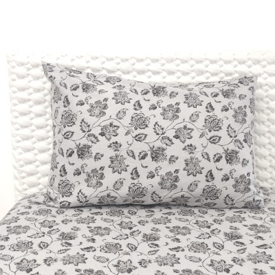 Fronha de almofada cinzenta com flores pretas sobre colchão e fundo branco acolchoado