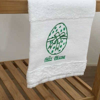 Toalha branca com bordado verde de ovo decorado e texto 'Feliz Páscoa'