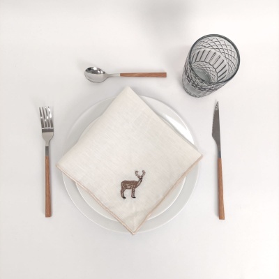 Conjunto de talheres com cabos em madeira, prato branco com guardanapo branco bordado, copo transparente e fundo branco.