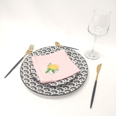 Conjunto de prato com guardanapo rosa bordado, talheres dourados e pretos e taça de vidro