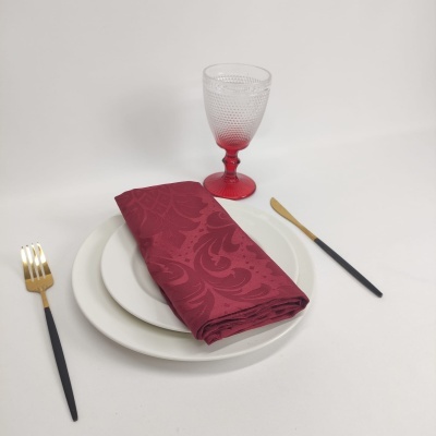 Conjunto de jantar com prato branco, guardanapo bordô, copo e talheres pretos e dourados