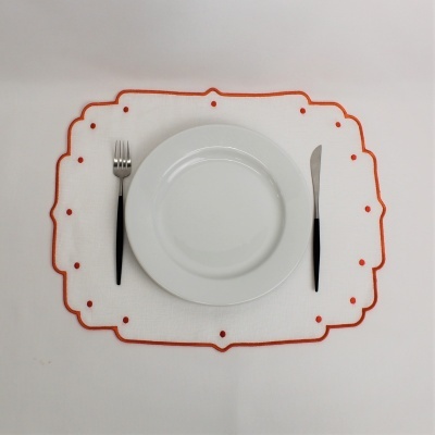 Lugar de mesa com prato branco, garfo e faca com cabos pretos, sobre individual branco com borda e pontos vermelhos