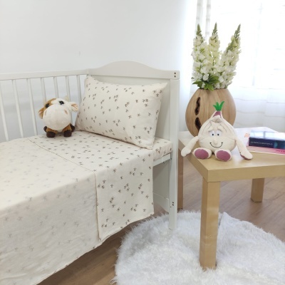 Cama de criança com roupa de cama bege floral e peluches, mesa amarela com peluche e flores