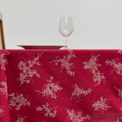 Toalha de mesa vermelha com padrão floral branco, cadeira de madeira, taça de vidro
