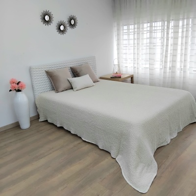 Cama com edredão cinza claro e almofadas castanhas e branca em quarto iluminado com vaso de flores e decoração de parede