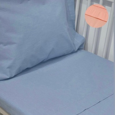 Jogo de lençóis azul claro com detalhe rosa salmon e bordado numa cama branca