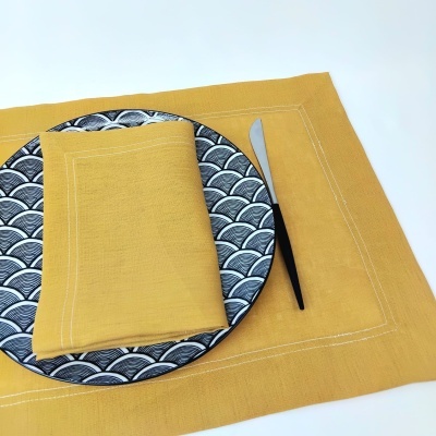 Conjunto de mesa com prato cerâmico com padrão em ondas pretas e brancas, guardanapo e toalha amarelos, faca com cabo preto.