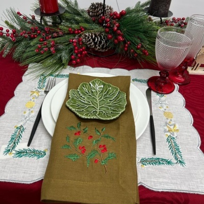 Mesa de Natal com pratos, guardanapo bordado, talheres pretos, copos de vidro vermelho e arranjo festivo