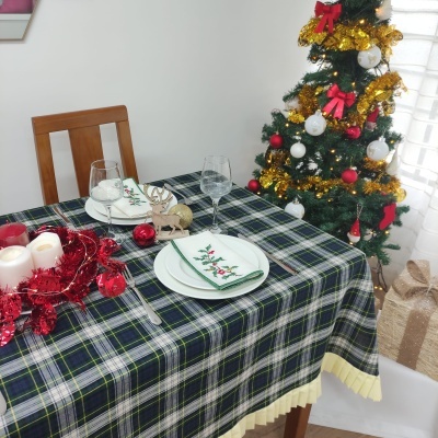 Mesa com toalha xadrez e decoração natalícia ao lado de árvore de Natal decorada