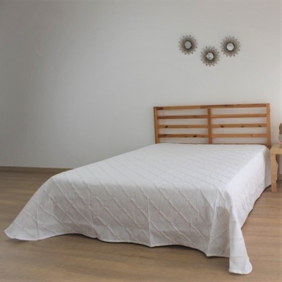 Cama de madeira clara com colcha branca e decoração de sol na parede