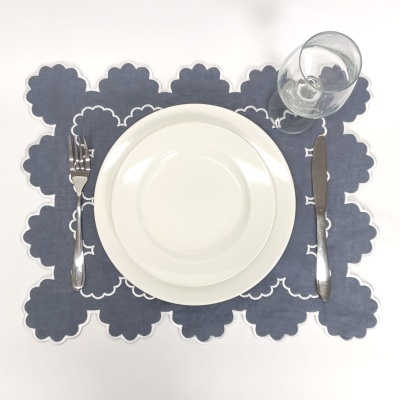 Conjunto de jantar com prato branco, talheres em aço inox, copo de vidro e individual azul de tecido com bordas brancas