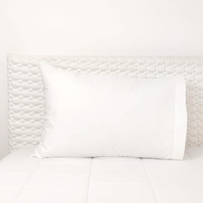 Travesseiro branco sobre cama branca com cabeceira acolchoada