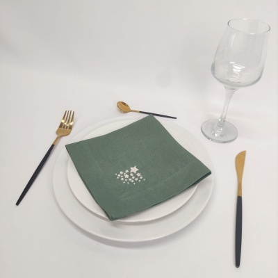 Conjunto de mesa com pratos brancos, guardanapo verde, talheres dourados e pretos e taça de vidro