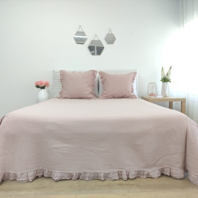 Cama de casal com colcha rosa clara e almofadas, em quarto minimalista com decoração simples e espelhos na parede