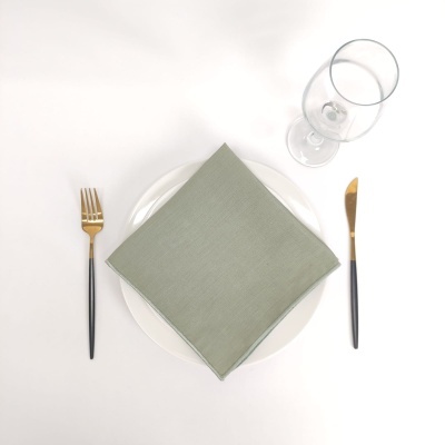 Conjunto de mesa com prato branco, guardanapo verde, talheres dourados com cabo preto e copo de vinho