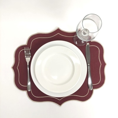 Conjunto de jantar com prato branco, sousplat bordô, talheres em metal e copo transparente