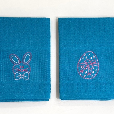 Duas toalhas azuis com bordados de coelho e ovo da Páscoa.