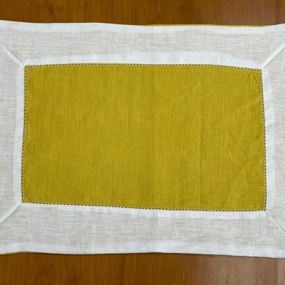 Toalha individual retangular com centro amarelo mostarda e borda branca em tecido sobre superfície de madeira.